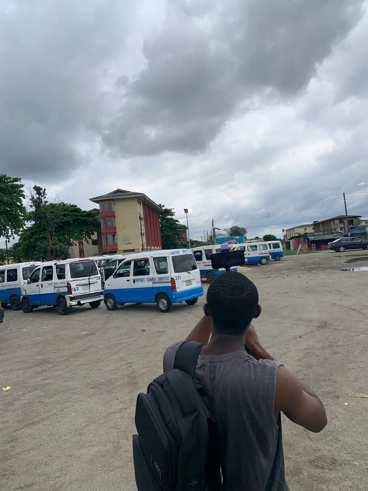odii from behind, filming the rows of uniport shuttles under a cloudy sky